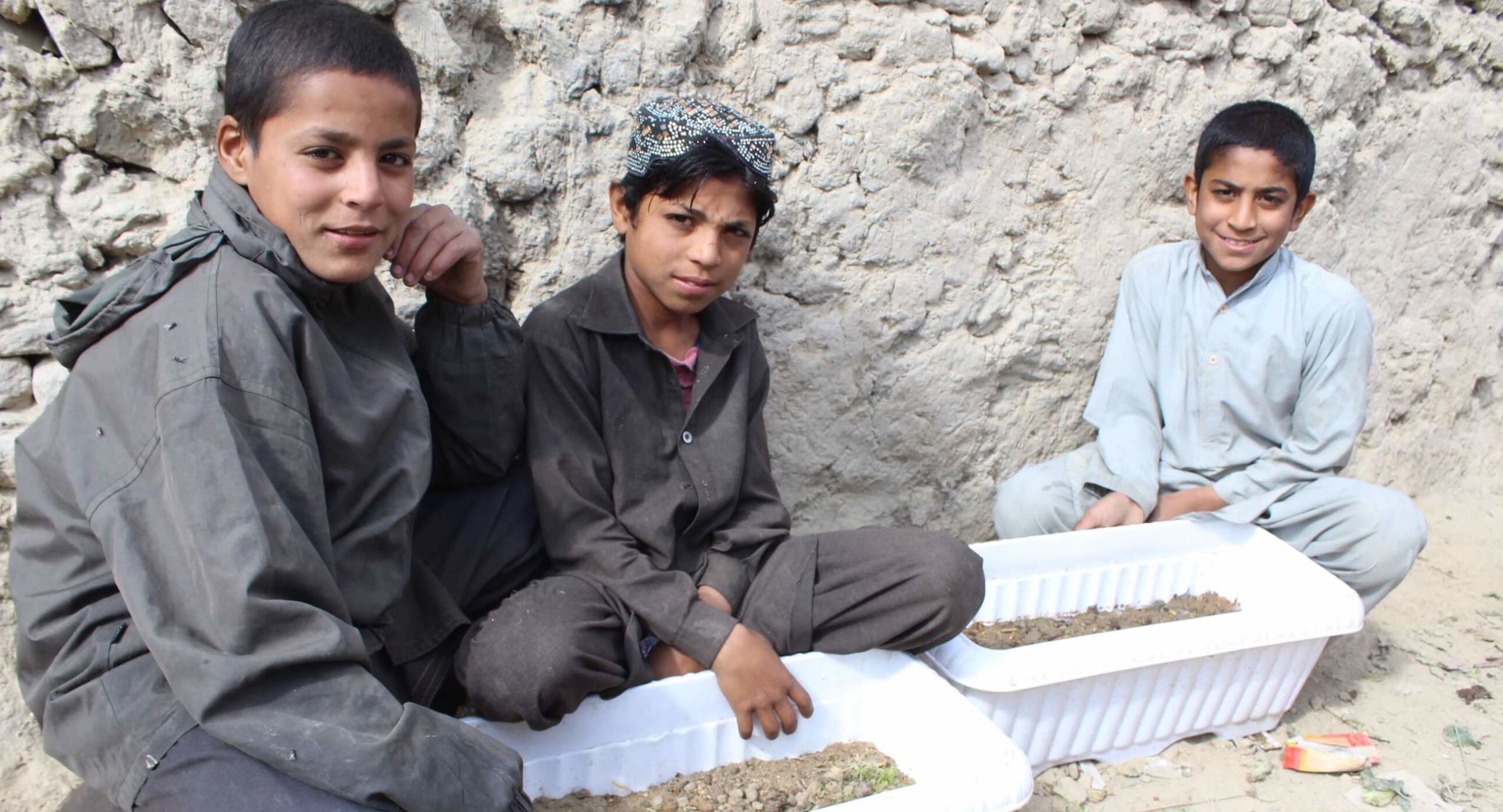 Three youth show off their permaculture planter boxes, as part of a workshop by NGO Afghan Peace Volunteers to help Afghan youth displaced by conflict to learn skills.